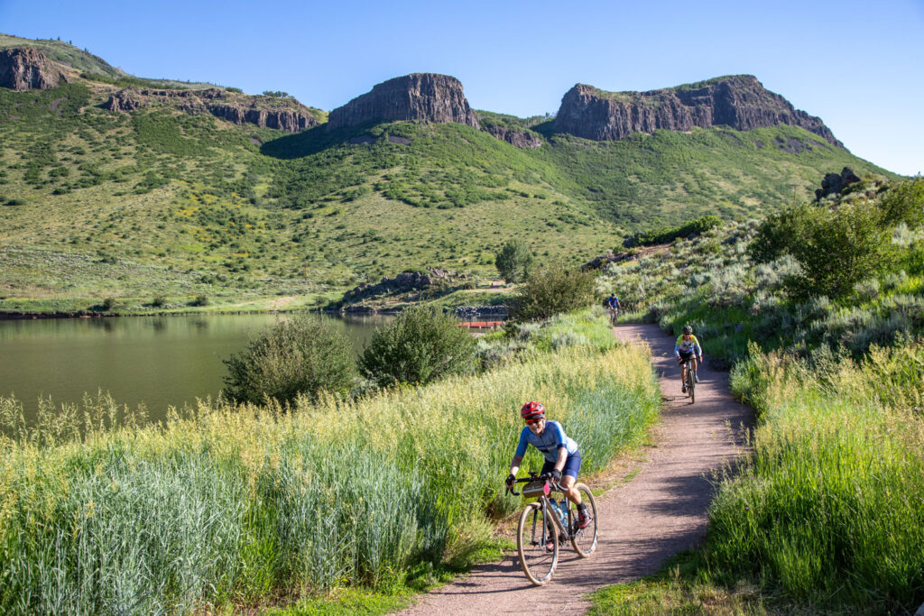 bike riders on path with lake and cliff background.