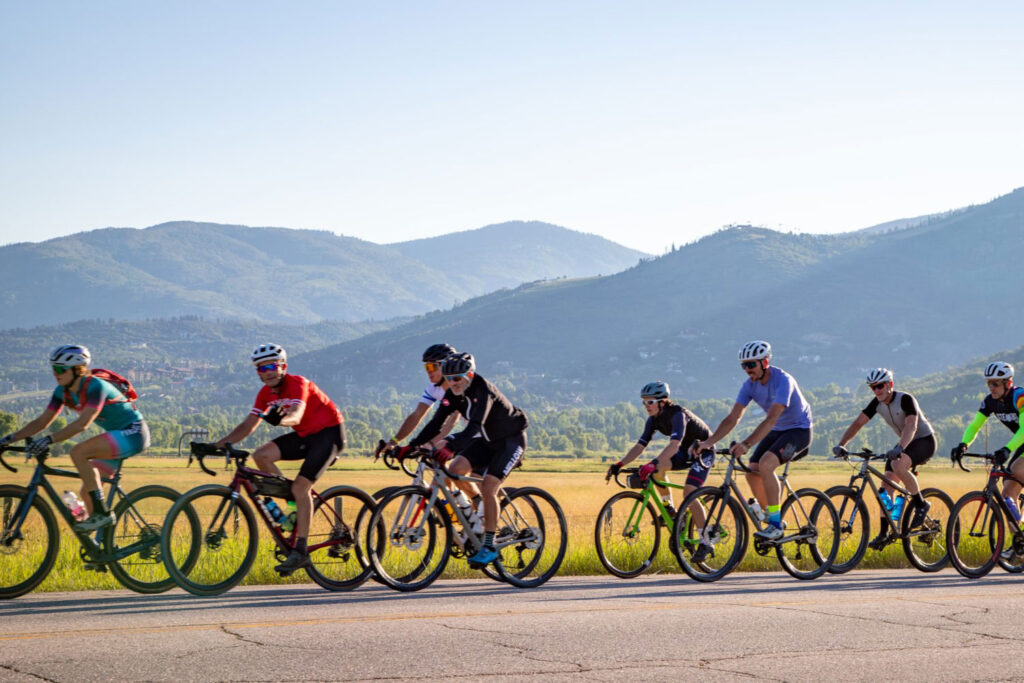 A line of bike riders on a road with mountain background
